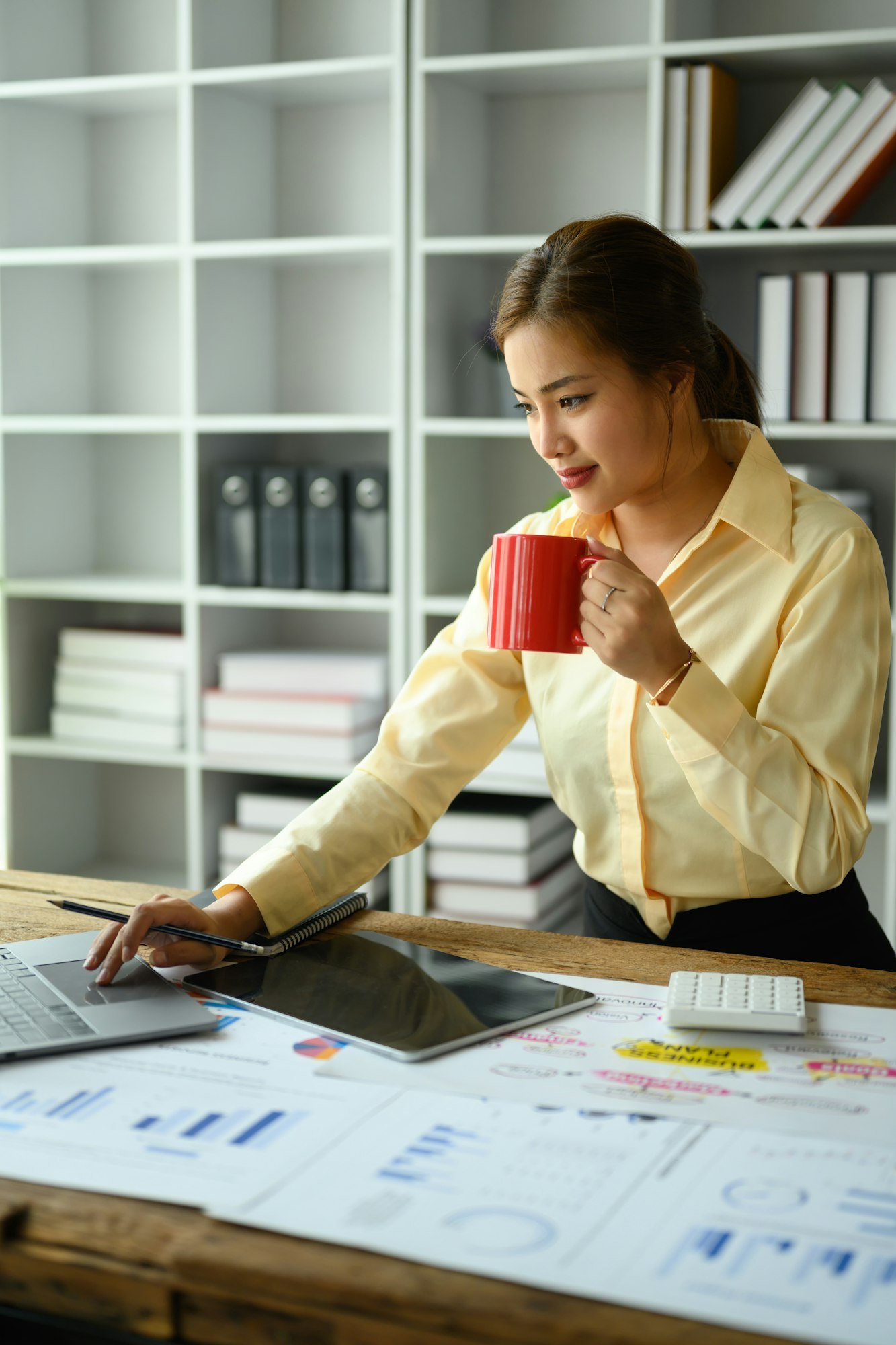 Image of female office worker holding coffee cup and checking business email on laptop computer.